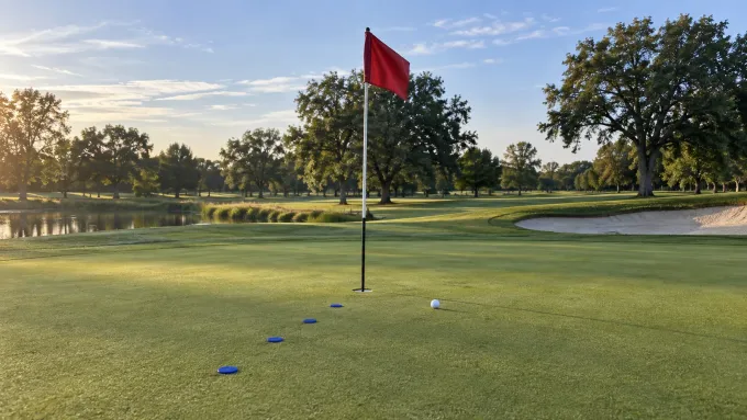 Original editorial image of an empty golf green with four blue markers leading toward one ball and a blank crimson flag.