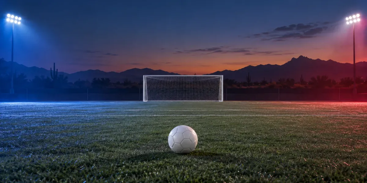 Original editorial image of one soccer ball on an empty field split between BYU blue and Arizona red beneath a desert dusk sky.