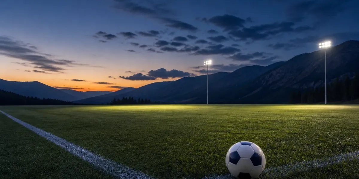 Original editorial illustration of one soccer ball on an empty mountain-backed field beneath two pools of stadium light.