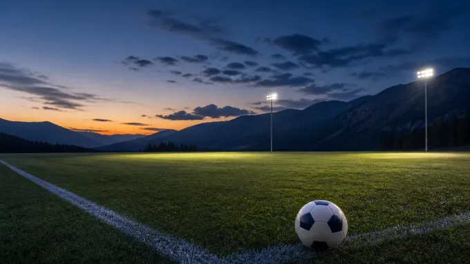 Original editorial illustration of one soccer ball on an empty mountain-backed field beneath two pools of stadium light.